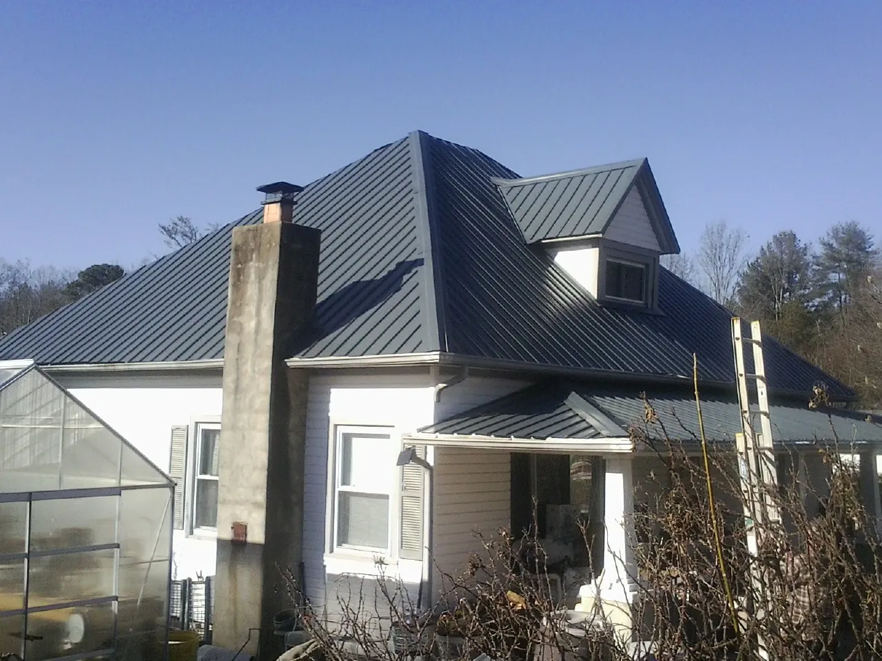 Dark blue standing seam metal roof on a white farmhouse with dormer — Slate & Tile Roof Repair by Roofing Brothers in Highland Park