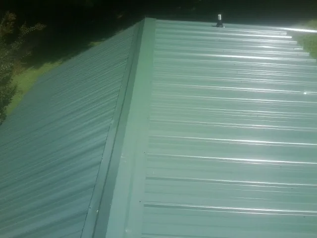 New green metal panels meeting at the ridge of a roof — Flat Roof Repair work by our crew in Highland Park