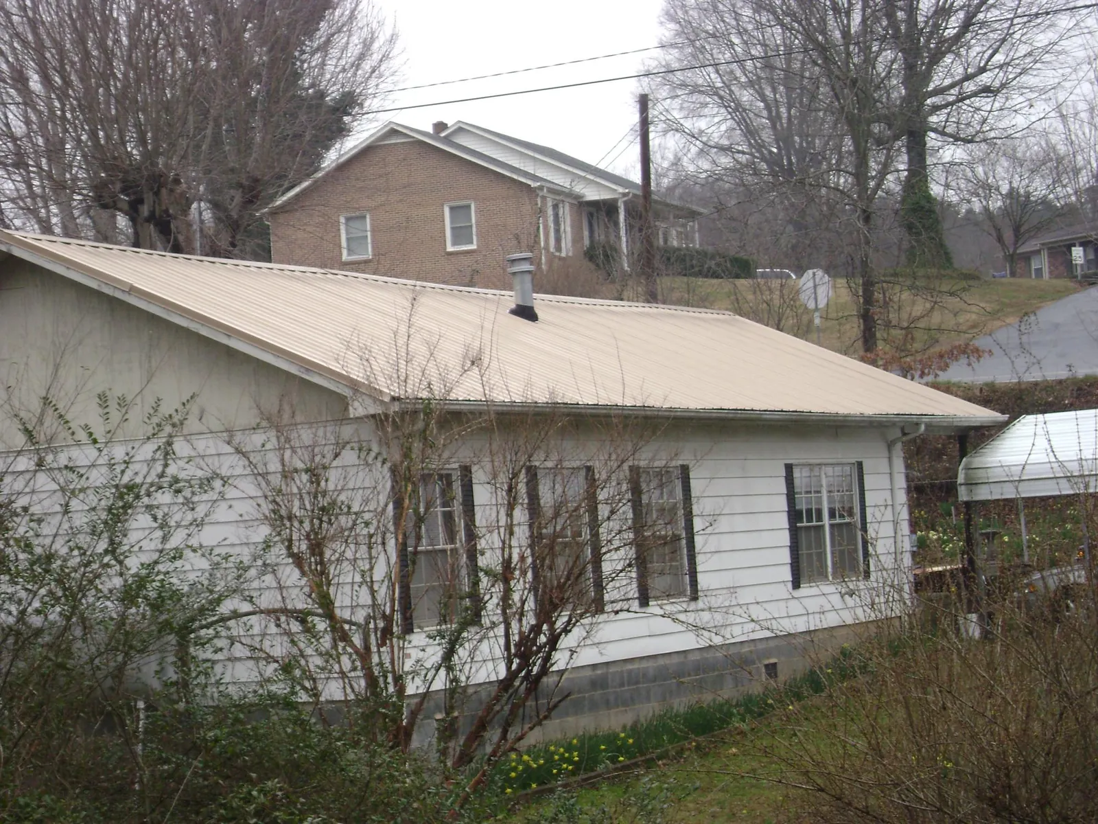 Tan metal roof on a white sided house set into a hillside — Commercial Roofing by Roofing Brothers in Highland Park